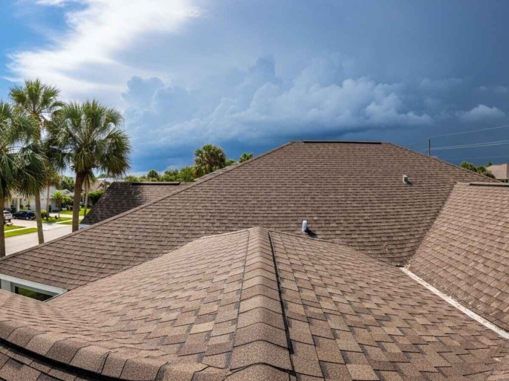 Florida home with aging asphalt shingle roof under strong sun and approaching storm clouds.