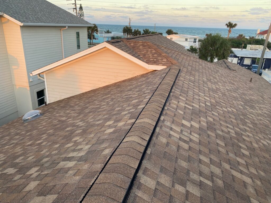 New brown Atlas Pinnacle Pristine shingles in Morning Harvest on a beachside home in Flagler Beach, FL, with ridge vent, a tubular skylight, and an ocean view in the background.
