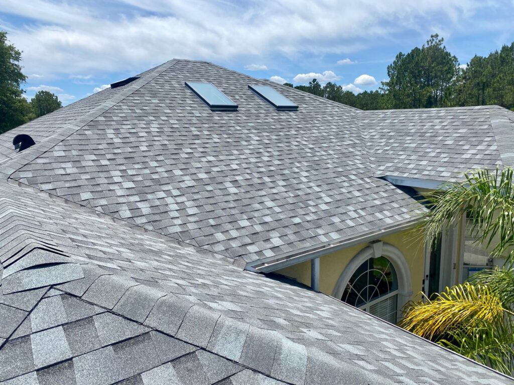Completed roof replacement on a yellow stucco home in Palm Coast, FL with gray Atlas Pinnacle Pristine shingles in Coastal Granite, two skylights, and hip ridge caps.