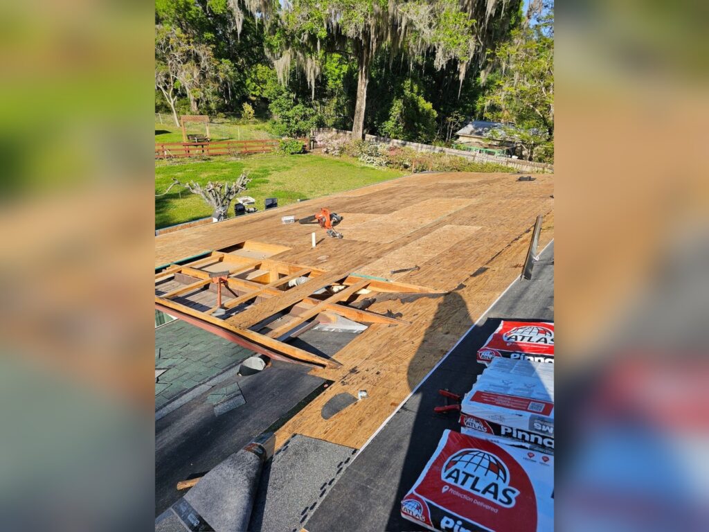 Roof replacement in progress in Pierson, FL, with new plywood decking, exposed rafter repairs, underlayment going down, and bundles of Atlas Pinnacle Pristine shingles staged on the roof.
